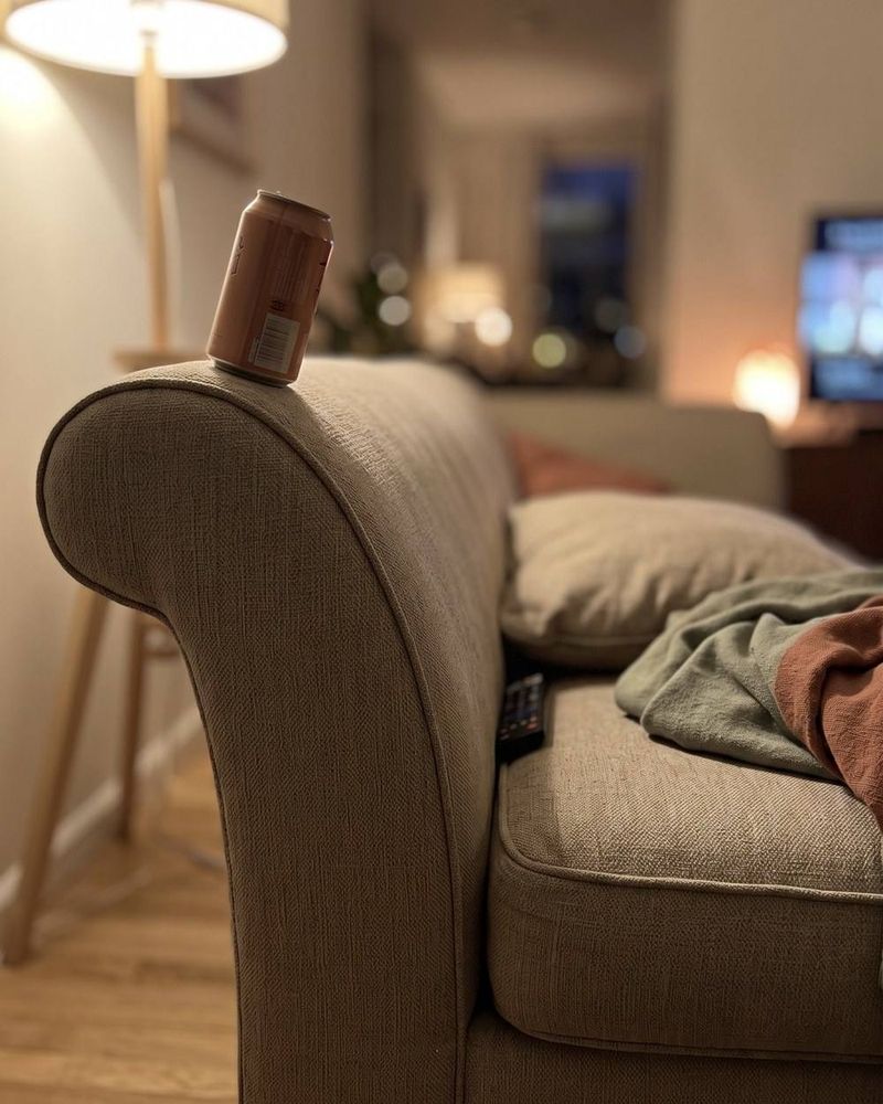 A can balanced on the rolled arm of a sofa.