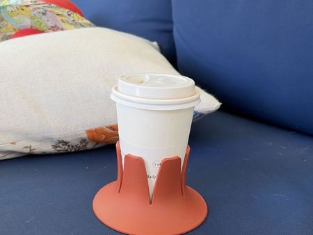 A paper coffee cup in a terracotta Steadi on a navy patio-sofa cushion in the sun.