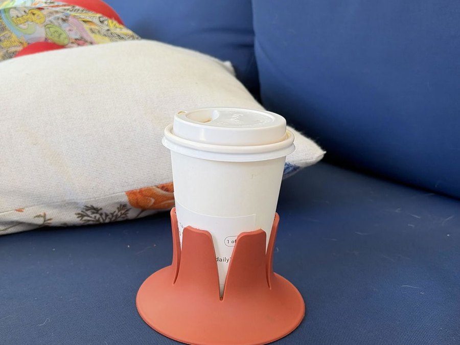 A paper coffee cup in a terracotta Steadi on a navy patio-sofa cushion in the sun.