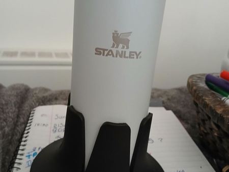 A white Stanley bottle seated in a black Steadi standing on an open planner.