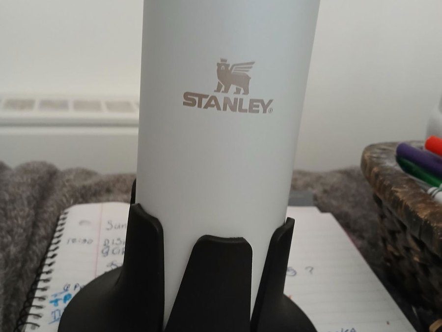 A white Stanley bottle seated in a black Steadi standing on an open planner.