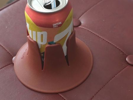 A soda can with a straw in a burgundy Steadi on a tufted leather ottoman.