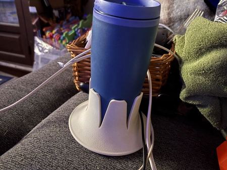 A blue travel tumbler in a cream Steadi on the arm of a grey couch at night.