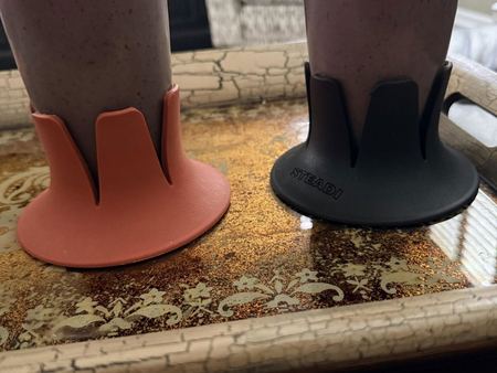 Two Steadis, one coral and one black, each holding a berry smoothie on a gold tray.