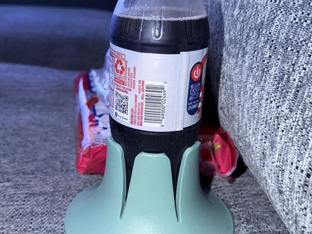 A plastic cola bottle in a mint Steadi on a grey woven couch cushion beside the arm.
